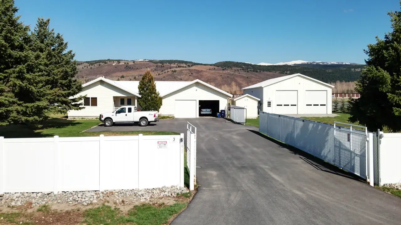 White vinyl fences and an open gate at the foot of the driveway, kennel buildings beyond