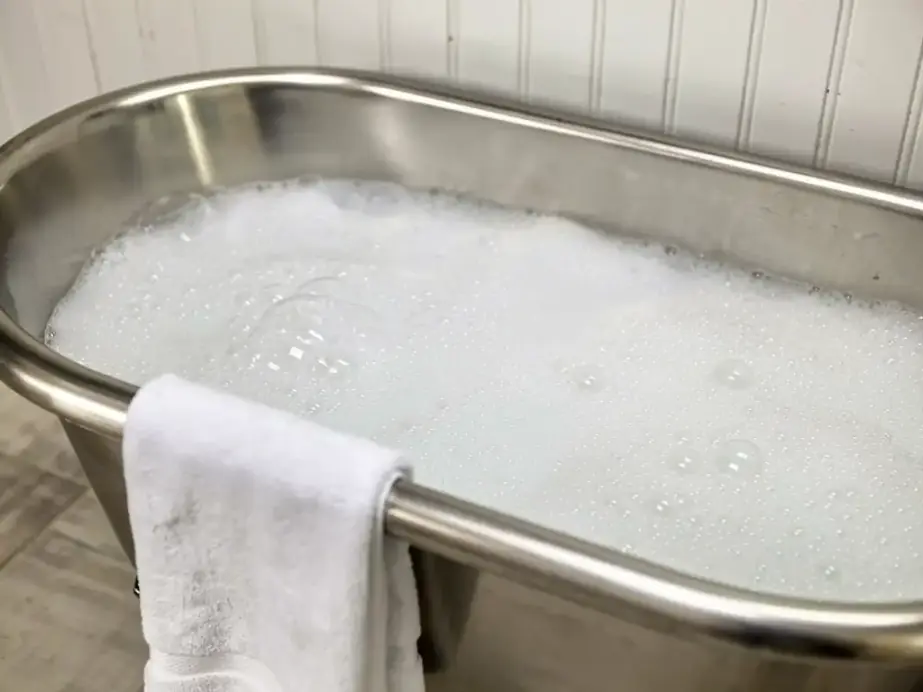 Stainless bathing tub filled with milky white microbubble water, a folded towel on the rim